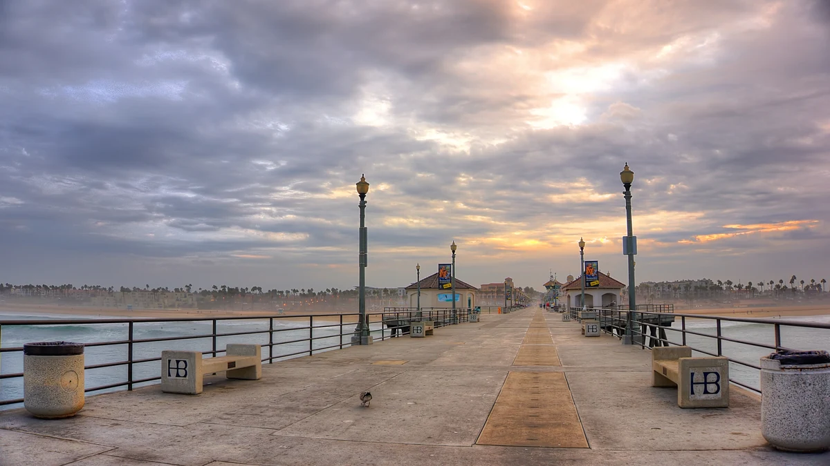 Huntington Beach Pier walkway, HB-marked benches, beach and town at sunrise. — destination photo, not the race course
